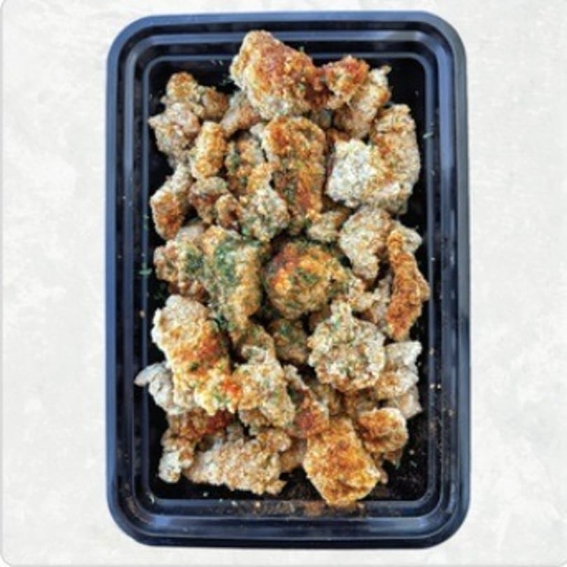 Crispy Asian-fusion popcorn chicken, seasoned with spices and herbs, in a black takeout container.