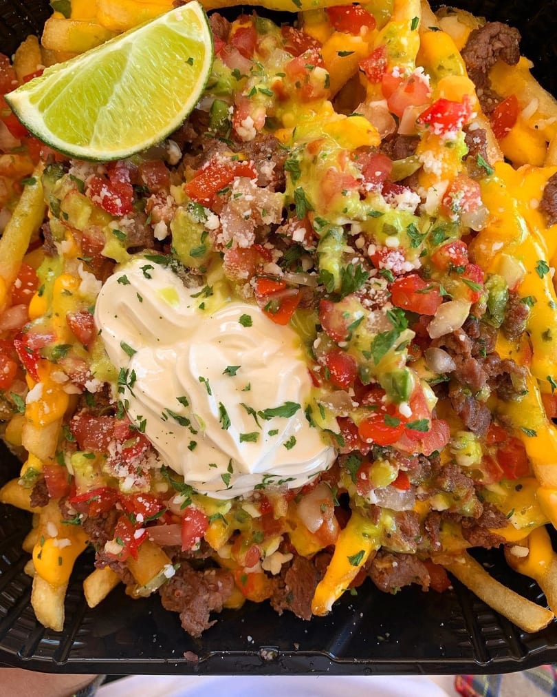 Loaded fries with cheese, ground meat, pico de gallo, sour cream, and a lime wedge.