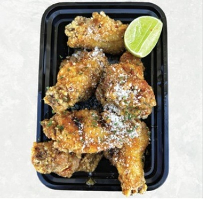 Crispy Asian-fusion chicken wings with lime and grated cheese in a black container.